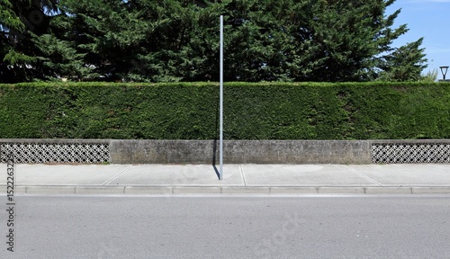 Wallpaper Mural Metallic pole on  sidewalk with concrete fence, hedge and trees on behind. Street in front. Background for copy space. Torontodigital.ca