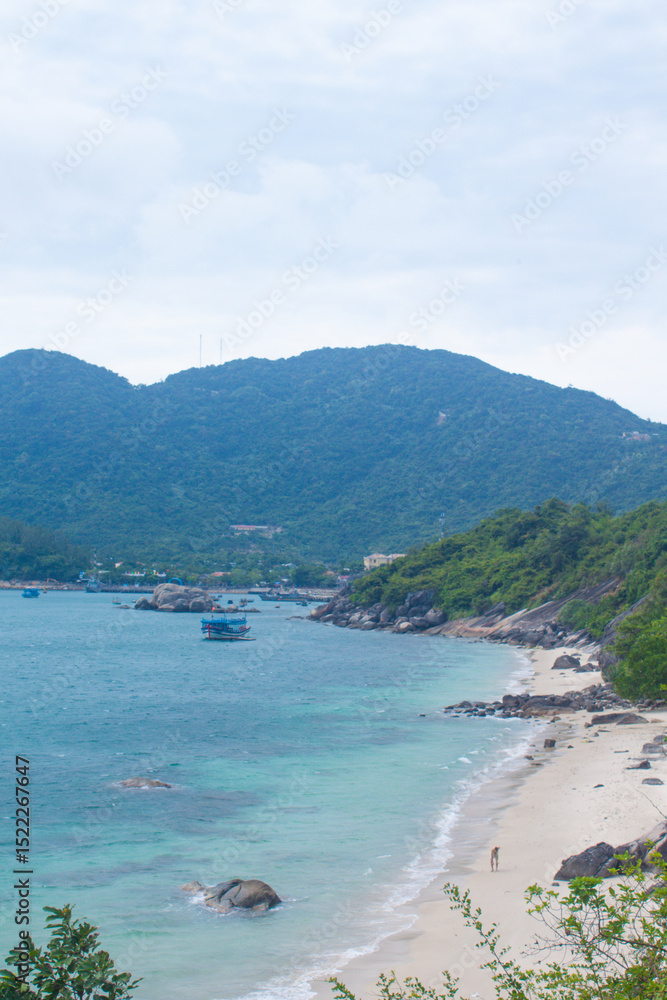 Obraz premium Scenic coastal view of Cham Islands with fishing boats, tropical mountains and a person walking along a deserted beach.