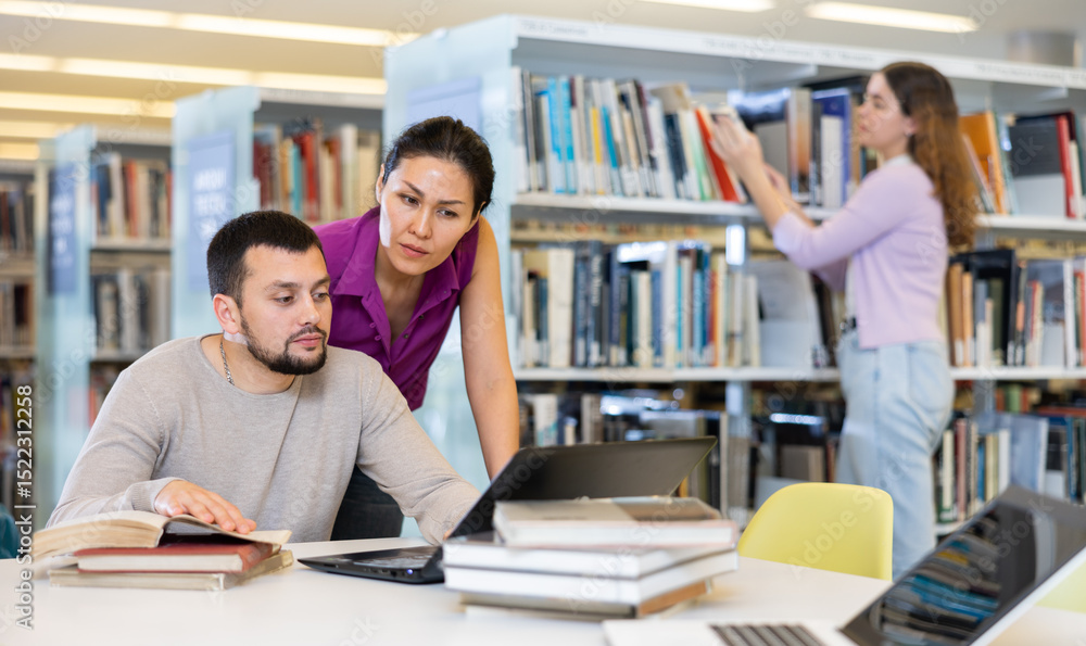 Woman and man looking at laptop screen together in public library Woman and man looking at laptop screen together in public library
