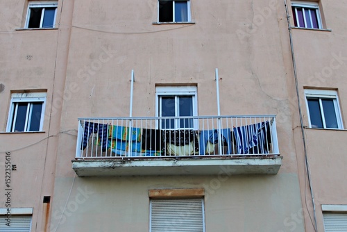 Residential balcony in Cádiz with colorful laundry hanging on a white railing, set against a worn pastel façade with visible cracks, windows and urban details typical of southern Spain.