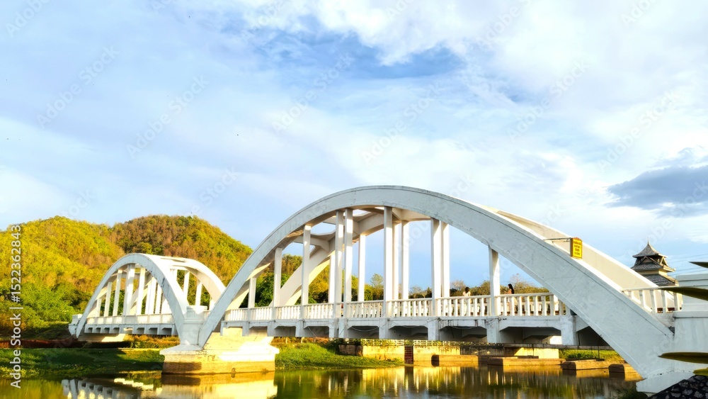 Obraz premium Elegant White Arch Bridge Against Scenic Hills and Blue Sky