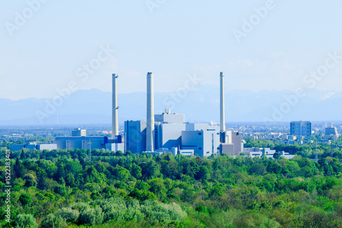 Modern power plant in the middle of a green landscape with a view of the Alps - symbol for energy production, global warming and change towards a sustainable environment - Munich, Germany