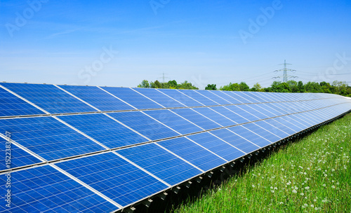 A modern solar plant in a green landscape with a high-voltage power line in the background, show the progress of sustainable energy production and the transformation to ecologically renewable energy