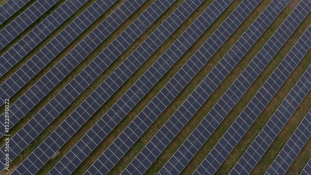 Drone shot of a photovoltaic solar farm with symmetrical diagonal rows of solar panels stretching across the terrain, illustrating clean energy production and sustainable infrastructure development. Drone shot of a photovoltaic solar farm with symmetrical diagonal rows of solar panels stretching across the terrain, illustrating clean energy production and sustainable infrastructure development.