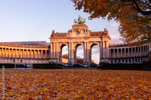 Fototapeta Naklejka Na Ścianę i Meble -  Low angle view of the Cinquantenaire Arcade at sunset in autumn, with fallen leaves covering the foreground