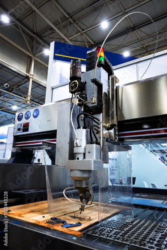 Fototapeta High-tech waterjet cutting machine head processing material on a production bed with safety guards and industrial signals, showcasing modern industrial manufacturing equipment