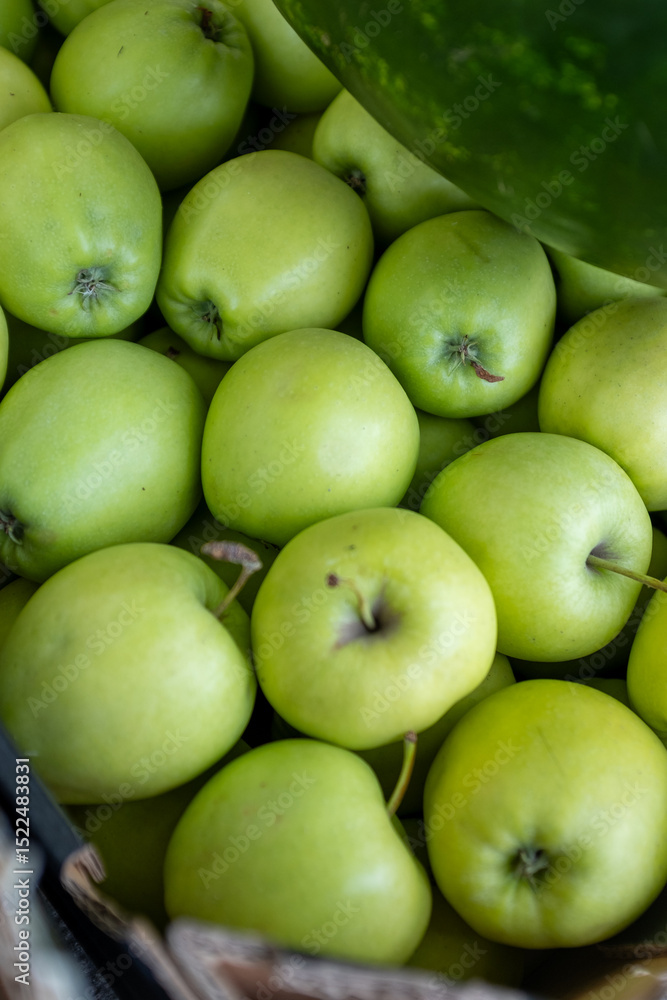 A close-up, top-down view of a bountiful display of vibrant green apples, likely Granny Smiths, partially obscured by a watermelon, highlighting fresh produce at a market A close-up, top-down view of a bountiful display of vibrant green apples, likely Granny Smiths, partially obscured by a watermelon, highlighting fresh produce at a market