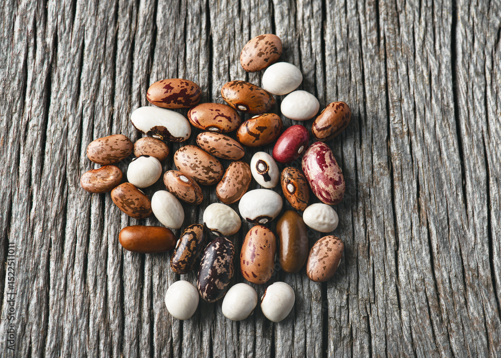 Obraz premium Top view of colorful mix dried legume beans (Phaseolus vulgaris) on rustic wooden background. Dried Legume Beans for Healthy Cooking concept.