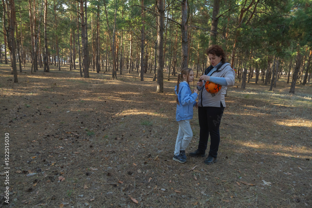 Fototapeta premium Grandmother and granddaughter walking in forest holding sports ball on sunny day