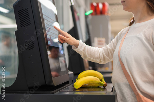 Faceless woman using self-checkout technology at grocery store. 