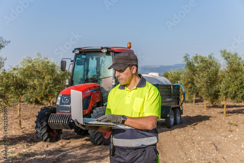 Man operating laptop in olive field in Andalucia, agricultural worker with tractor background