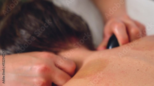 Closeup view of hot stone massage with smooth black stones placed on bare back during a relaxing therapy session. Perfect for spa, wellness, healing, and alternative health care concepts. 