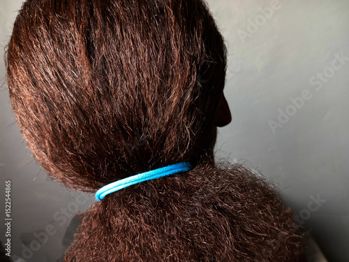 Back view of neatly combed and tied pony natural brown permed hair of an African woman after unbraiding twisted or cornrow braided hair.