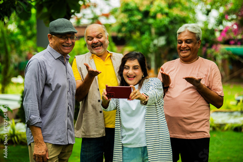 Canvas Print Checking photos on smartphone, elderly Indian group smiles while standing in lus