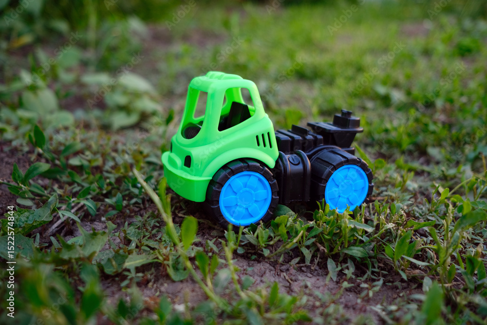 Fototapeta premium A bright green toy truck rests on the lush grass showcasing its vibrant colors Sunlight illuminates the scene creating a playful atmosphere perfect for outdoor adventures