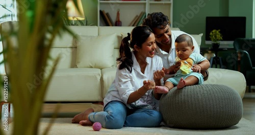 Parents sitting with baby boy while sitting on floor near sofa in modern living room, showcasing Indian family bonding, love, parenting, parenthood, emotional care, happy lifestyle, and cozy moments
