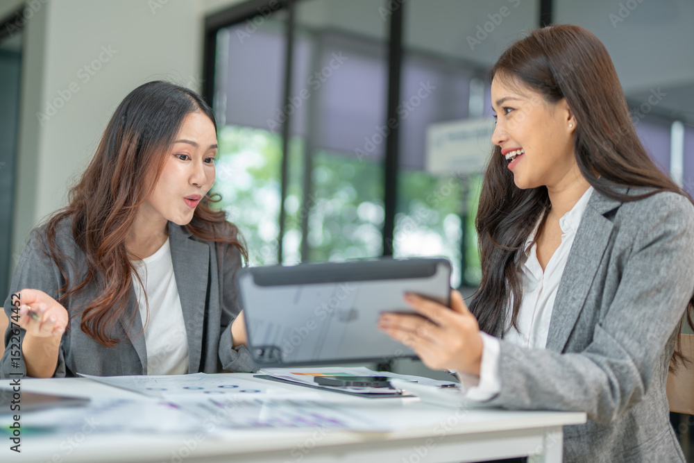 Two professional businesswomen are working on laptop computers sitting at desks in the office. Colleagues are happy and discussing the digital strategy of the Graph Two professional businesswomen are working on laptop computers sitting at desks in the office. Colleagues are happy and discussing the digital strategy of the Graph