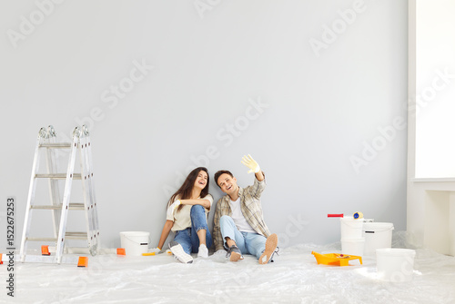 Young and happy family couple, sitting on floor and dreaming about new home during renovation and painting walls. Showing joy and excitement about construction and home improvement.