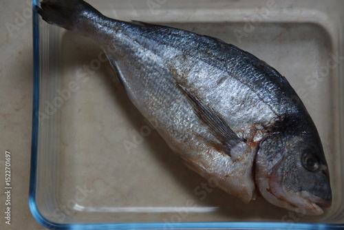 A raw sea bream, fresh and ready to be cooked. Its pearly flesh and shiny skin reflect its quality and freshness.
