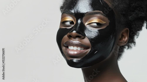 Black clay facial mask application with golden eye makeup