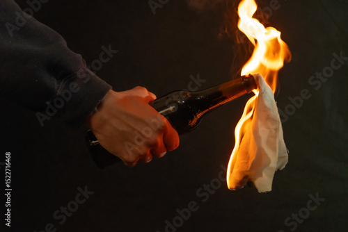 A hand holding a bottle with a burning rag against a dark background - symbolic of street protest or conflict.