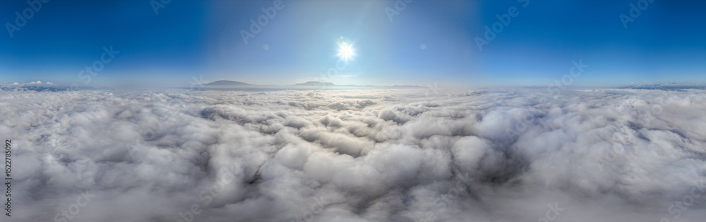 Naklejka premium A serene view of the early morning sun rising above a vast sea of clouds, with distant mountain peaks faintly visible on the horizon, creating a peaceful and ethereal landscape. Flying over the cloud
