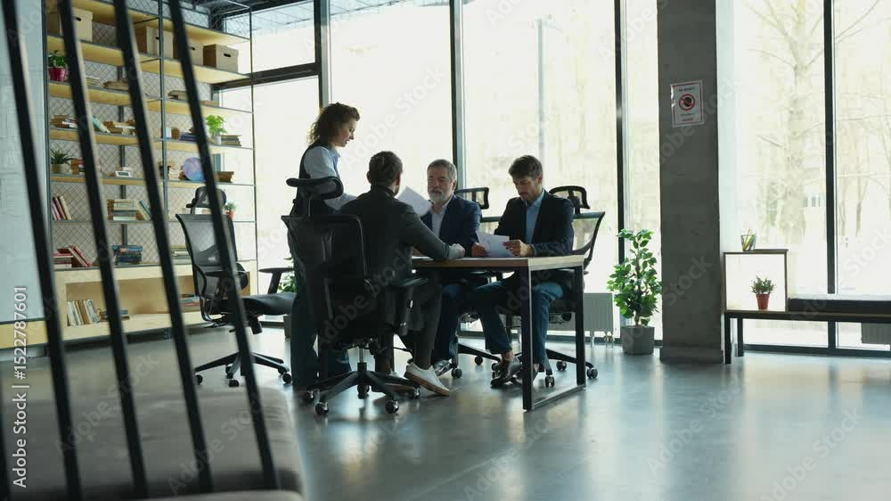 Confident female team leader boss supervisor standing at working desk holding paper documents talking to motivated interested focused teammates colleagues in modern office Confident female team leader boss supervisor standing at working desk holding paper documents talking to motivated interested focused teammates colleagues in modern office