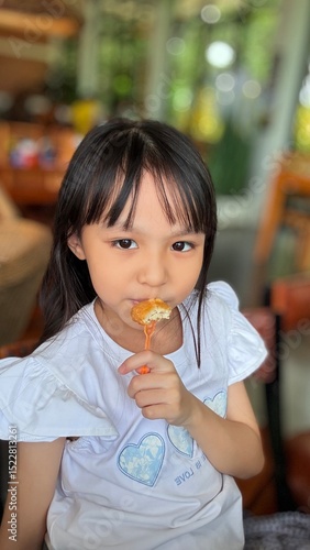 Happy cute Asian little girl holding fried chicken nugget to eat in restaurant, kid enjoying fast food concept.
