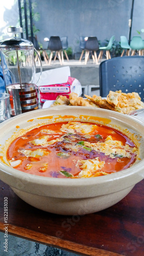Spicy Asian soup served in a clay pot, filled with fresh red broth, soft tofu, vegetables, and chili oil. Culinary concept, restaurant, or traditional food.