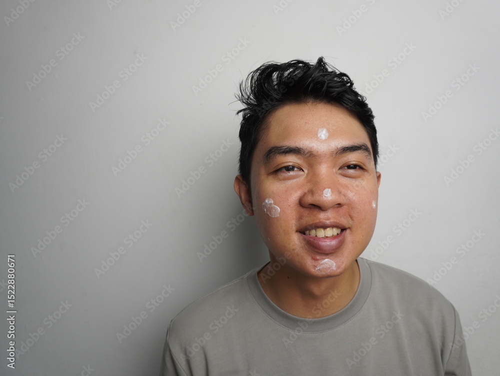 Happy asian man using cream or sunscreen on his face. Skincare concept Happy asian man using cream or sunscreen on his face. Skincare concept