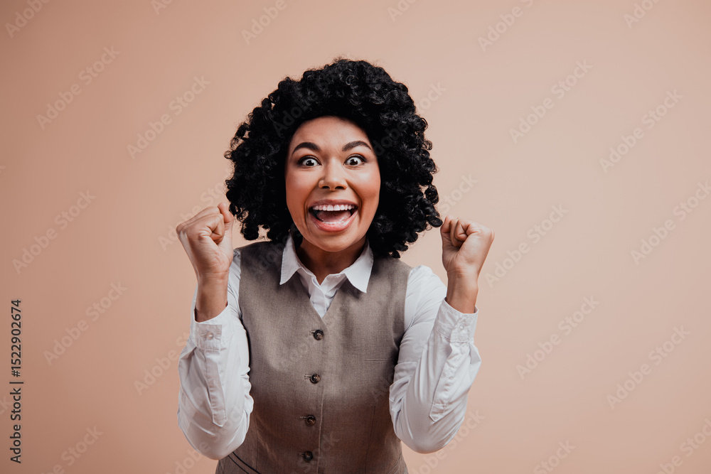 Fototapeta premium Portrait of a cheerful professional woman celebrating a success against beige background, expressing accomplishment and joy