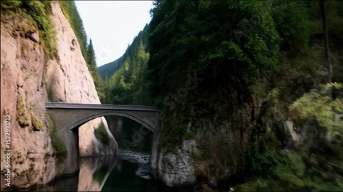 Serene river flows through lush green forest with rocky cliffs and an arch bridge connecting verdant banks, creating tranquil nature scene