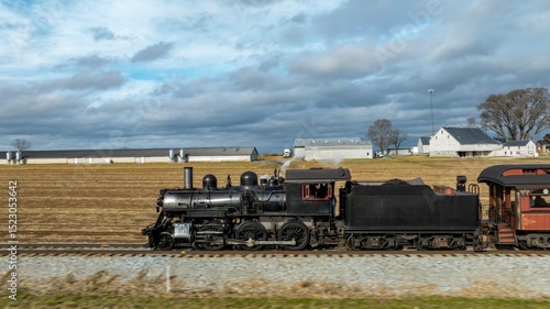 Wallpaper Mural A classic steam train rolls along tracks beside vast farm fields under a cloudy sky, showcasing a nostalgic journey through the countryside. The train exudes an old-fashioned charm. Torontodigital.ca
