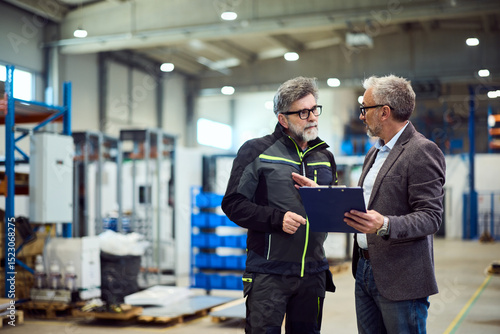 Two Professionals Discussing Work Within a Spacious Industrial Warehouse Setting