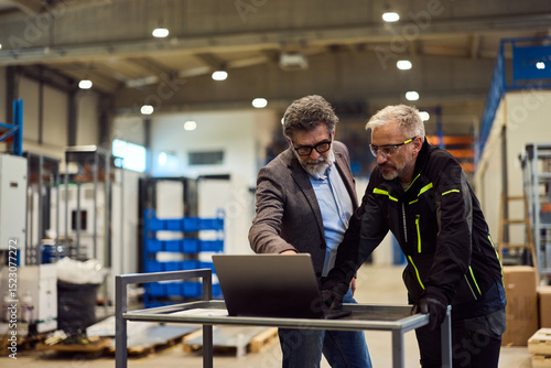 Two Professionals Discussing on a Laptop in a Modern Factory Floor