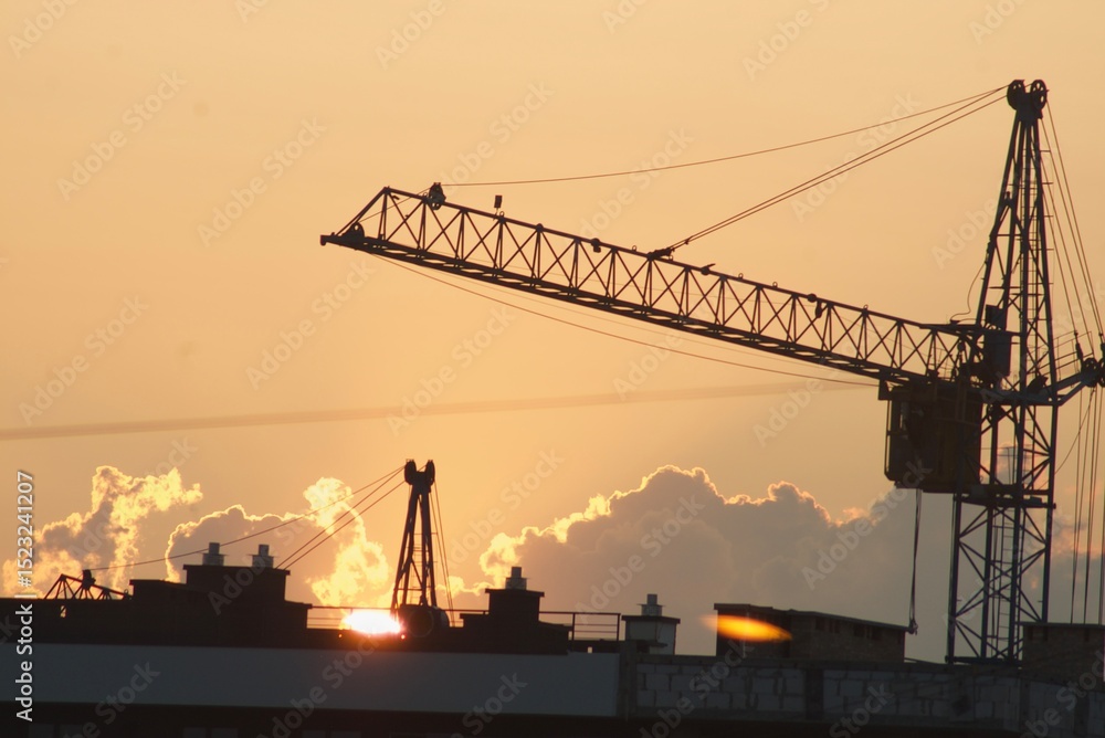 Obraz premium Sanset over city with silhouette of construction crane and building.