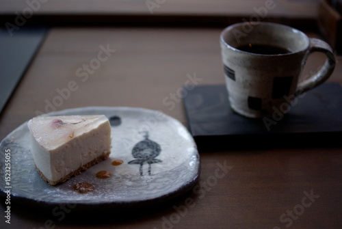和柄の陶器皿に載ったチーズケーキと窓辺のコーヒーセット


