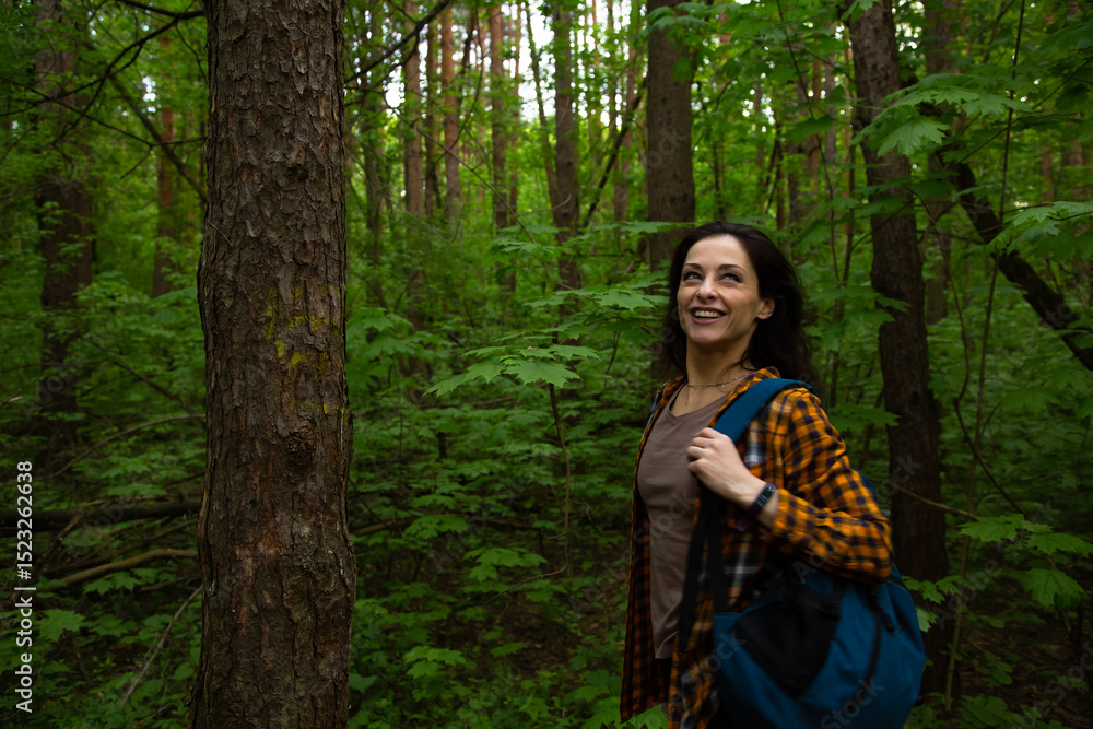 Beautiful smiling happy woman walking in a green forest on sunny summer weather. Girl relax standing in woods, in style fashion clothes near trees Beautiful smiling happy woman walking in a green forest on sunny summer weather. Girl relax standing in woods, in style fashion clothes near trees