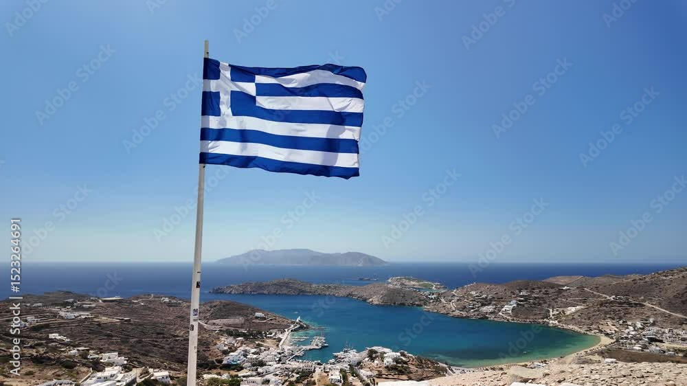 View of the Greek national flag overlooking the picturesque port of Ios Greece and the island of Sikinos in the background in slow motion
