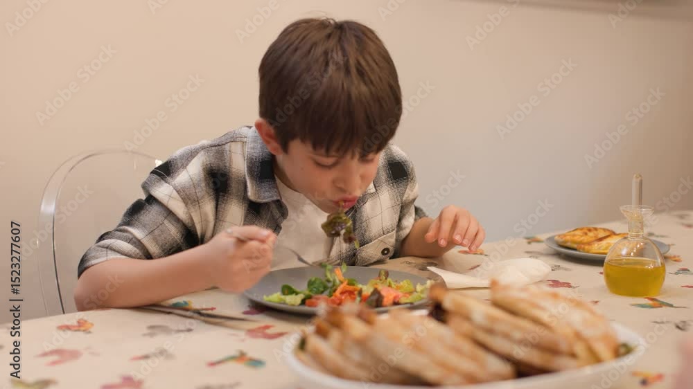 Medium shot of a boy seated at the dining table eating salad with visible appetite. Realistic image style with authentic expression and natural lighting. Real people, daily family moment.Horizontal 4K Medium shot of a boy seated at the dining table eating salad with visible appetite. Realistic image style with authentic expression and natural lighting. Real people, daily family moment.Horizontal 4K