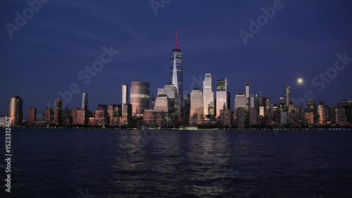 nyc skyline view of downtown manhattan skyscrapers at sunset dusk blue hour (glow glowing reflection from buildings) moving water flowing hudson river moonrise moon shining last light buildings nj