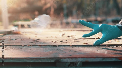 Hand in blue latex glove flicking crumpled plastic cup with finger snap off wooden picnic table slow motion spring sunset