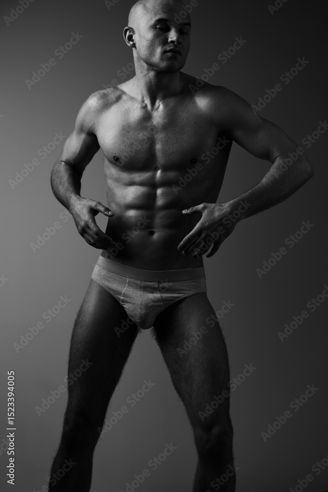 Fototapeta premium Muscular man posing confidently in black and white, showcasing strength and fitness in an artistic manner with dramatic lighting.