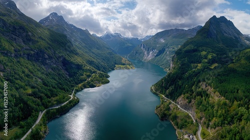 A bird's-eye view of the fjord, surrounded by towering mountains, green valley walls and a winding road leading to snow-capped peaks in the distance, offers panoramic views.