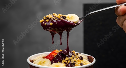 Close-up of an açaí spoonful with dripping textures and highlighted toppings, set against a dark background for visual focus and striking shadow contrast