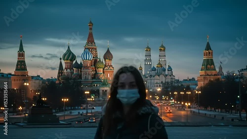 Woman wearing a mask stands in front of St. Basil's Cathedral at dusk in Moscow, Russia