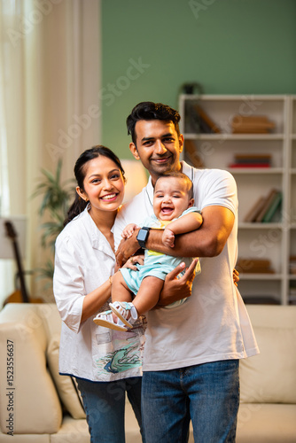 Young Indian parents standing with baby boy in arms inside modern stylish living room at home