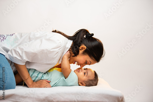 Фотография Smiling Indian parents interact joyfully with newborn baby boy lying on soft whi