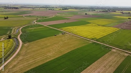 Aerial view of farmland with tractors, fields of crops, and a winding dirt road on a sunny day