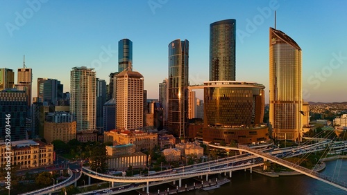 Fototapeta Naklejka Na Ścianę i Meble -  Brisbane CBD, Queensland, Australia, May 22, 2025: Aerial Sunset Image Featuring City Skyline, Skyscrapers, Brisbane River, The Wheel of Brisbane, and South Bank Cultural Precinct in Warm Evening